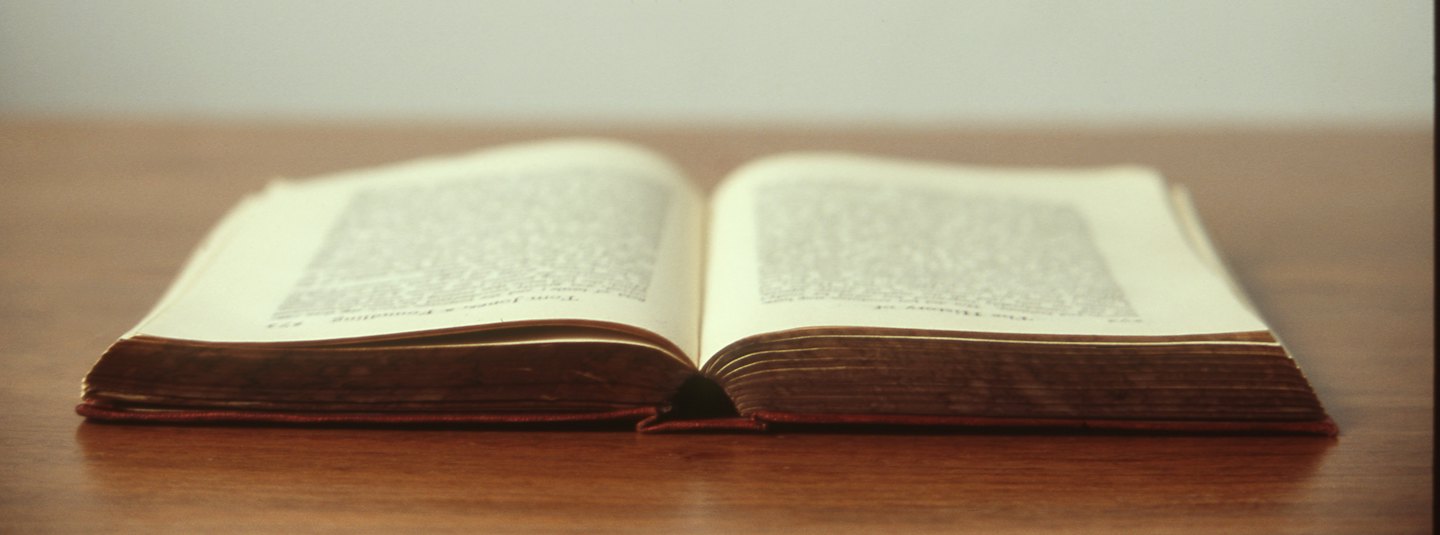 An open, aged book lies on a polished wooden table.