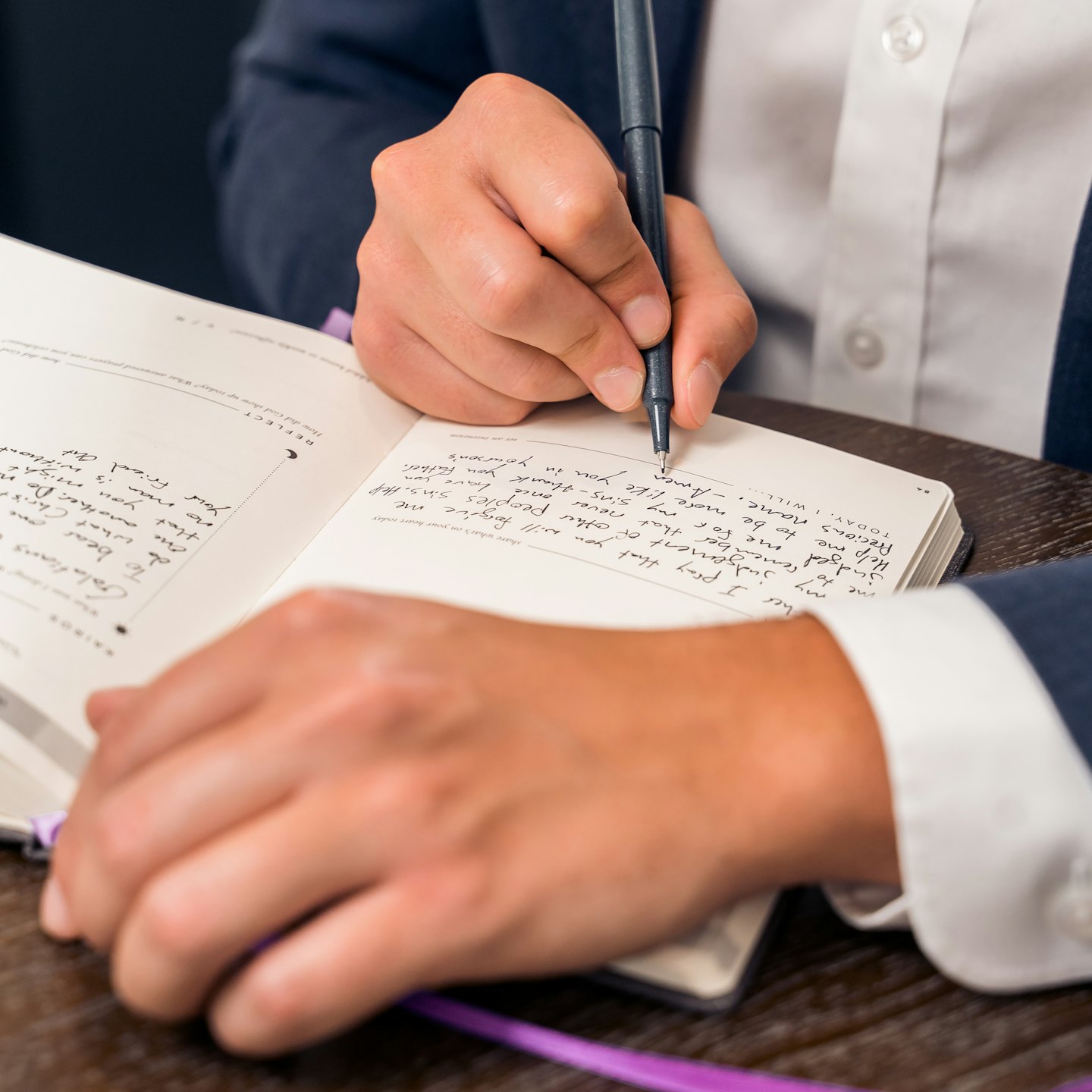 Person writing in a journal with a pen.